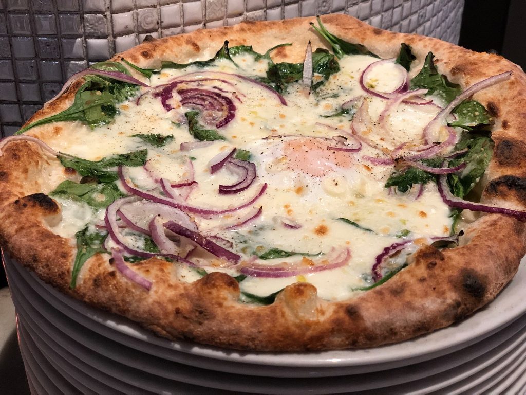 A pizza with onions and spinach on a plate
Description automatically generated