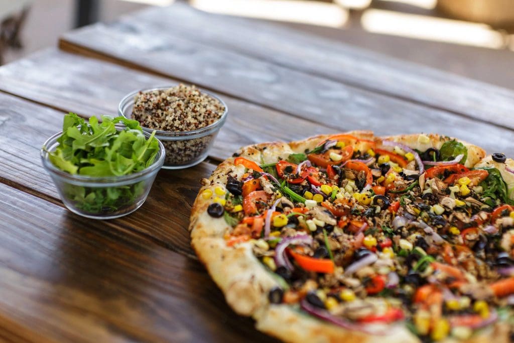 A pizza with vegetables and a bowl of salad
Description automatically generated
